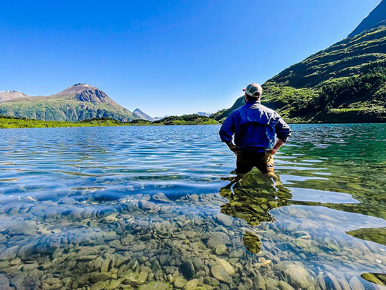 A person stands thigh deep in crystal clear water.