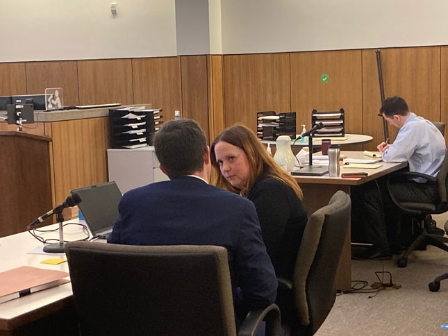 Assistant Attorney General Erin McCarthy and District Attorney Mark Clark face eachother, seated in a courtroom. Defendant Jordan Joplin is seated at a desk in the background.